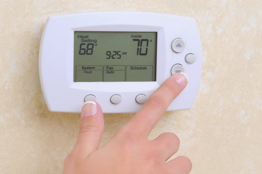 Closeup of a womans hand setting the room temperature on a modern programable thermostat